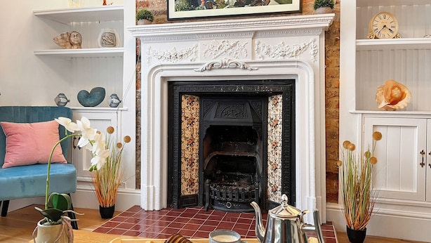 A cozy living room with a fireplace, a blue sofa, a tray with pastries and coffee, and decorative items on shelves. - This property is completely unique. (Scarborough)