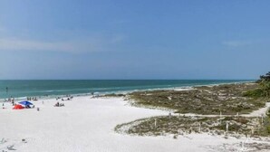 Una playa de arena blanca, cielo azul despejado y mar tranquilo.