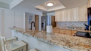 Una cocina moderna con encimeras de granito, electrodomésticos de acero inoxidable y armarios de madera clara.