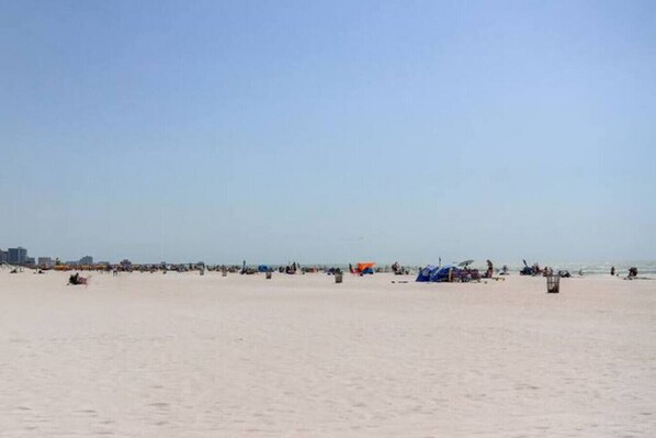 Una amplia playa arenosa con tiendas de campaña y gente dispersa.