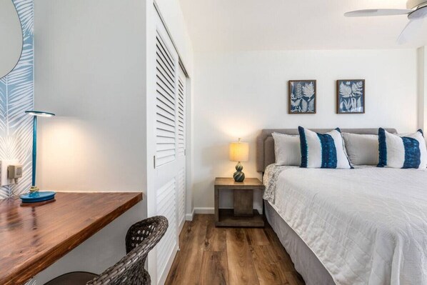 A bedroom with a bed, a nightstand with a lamp, a wooden desk, and a chair.
