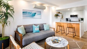 Een moderne woonkamer met een grijze bank, een bijzettafeltje en een grote potplant.