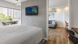 Een moderne hotelkamer met een groot bed, een flatscreen-televisie bevestigd aan een gestructureerde wand en een balkon met zitplaatsen.