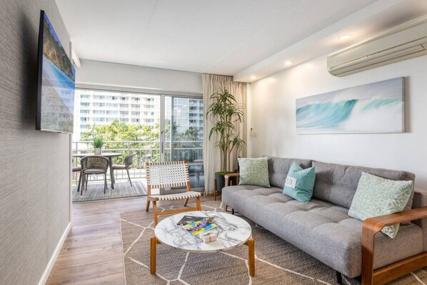 A modern living room with a grey sofa, wooden coffee table, and a balcony with outdoor furniture.