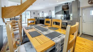 A modern kitchen with wooden furniture, a dining table with black placemats, and a staircase leading to an upper level. - 3 bedroom accommodation in Tregaron (Tregaron)