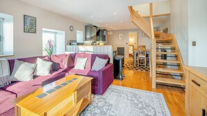 A modern living room with a purple sectional sofa, a wooden coffee table, and a staircase leading to an upper level. - 3 bedroom accommodation in Tregaron (Tregaron)