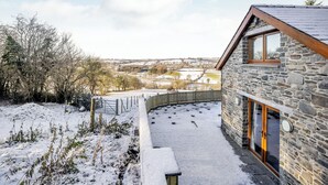 A stone building with a wooden roof and a glass door, surrounded by snow-covered ground and a view of a rural landscape. - 3 bedroom accommodation in Tregaron (Tregaron)