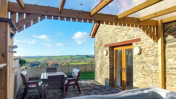 A wooden deck with a hot tub, stone walls, and a view of the countryside. - 3 bedroom accommodation in Tregaron (Tregaron)