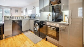 A modern kitchen with stainless steel appliances, a built-in washing machine, and a wooden floor. - 3 bedroom accommodation in Tregaron (Tregaron)