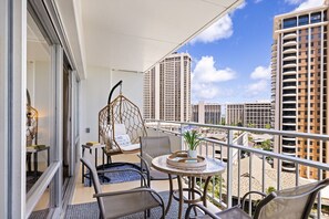 Ein Balkon mit Korbmöbeln, einem Hängesessel und einem kleinen Tisch mit einer Pflanze.