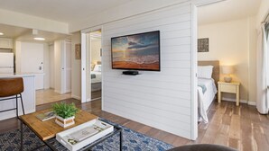 Ein modernes Wohnzimmer mit einem an der Wand montierten Flachbildfernseher, einem Couchtisch mit Pflanze und einem Bett mit Nachttischlampe.