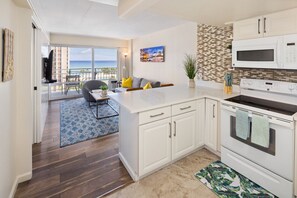 A modern kitchen with white cabinets, a microwave, and an oven. There is a dining area with a blue rug and a view of the ocean through large windows. - 1016 · Ilikai Collection # 4. Amazing views, beachfront. (Honolulu)