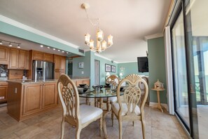 Una cocina con armarios de madera, un refrigerador de acero inoxidable, una mesa de comedor de vidrio con sillas y una araña.