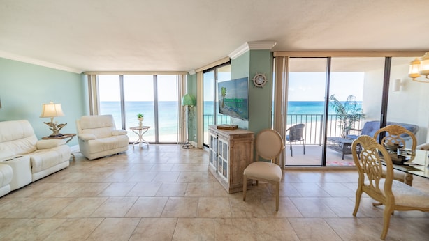 A spacious living room with a large TV, comfortable seating, a wooden cabinet, and a view of the ocean through large sliding doors. - Beach Blessings Edgewater 0602T2 Beautiful condo with Beautiful views! (Panama City Beach)
