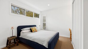 A bedroom with a bed, a bedside table, a lamp, a window, and a door.