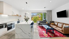 Una cocina moderna con una isla de mármol, una zona de comedor con alfombra roja, un sofá de cuero y un televisor montado en la pared.