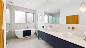 Un baño moderno con una bañera independiente, un espejo grande y un tocador doble.