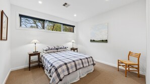 A bedroom with a large bed, two bedside tables, a chair, a window, and a painting on the wall.