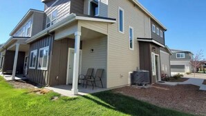 A two-story house with a covered porch, a garage, and a small yard with grass and mulch. - Convenient 3-Bedroom Townhome with Full Garage (Nampa)