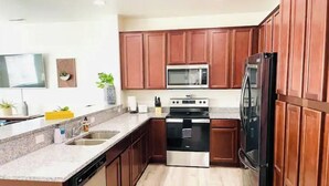 A modern kitchen with wooden cabinets, stainless steel appliances, and a granite countertop. - Convenient 3-Bedroom Townhome with Full Garage (Nampa)