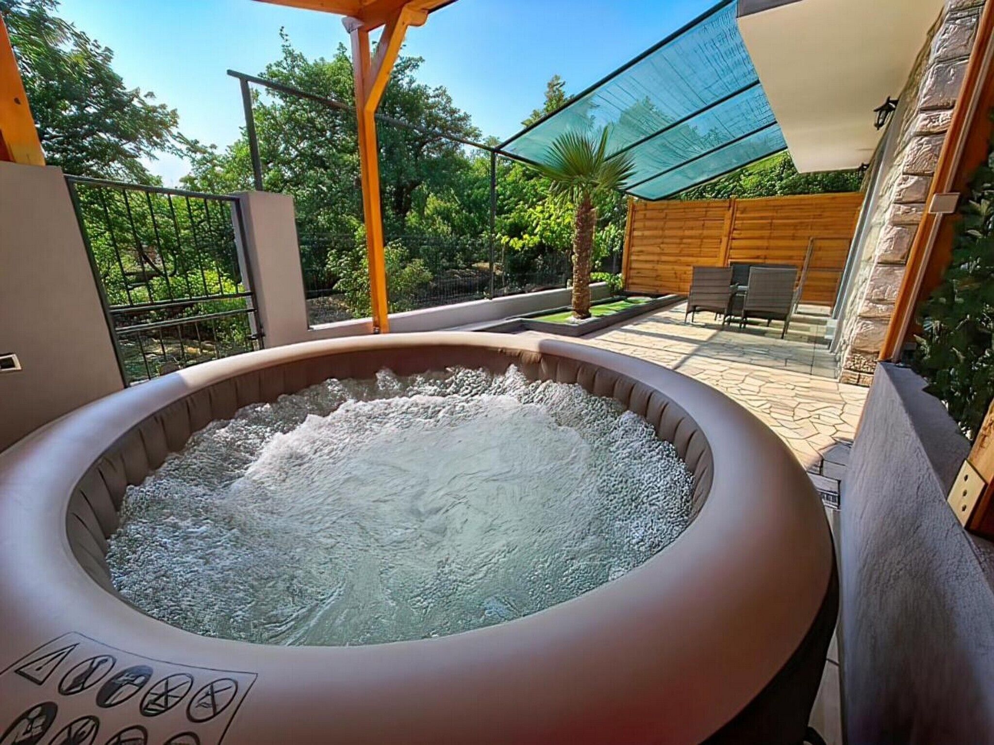 A hot tub in an outdoor setting with a patio area, wooden fence, and greenery.