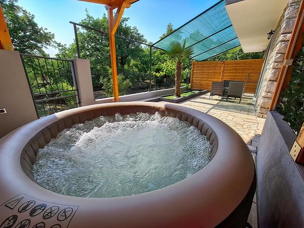 A hot tub in an outdoor setting with a patio area, wooden fence, and greenery.