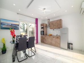 A modern kitchen with wooden cabinets, a stainless steel refrigerator, and a dining area with a glass table and chairs.