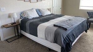Un dormitorio con cama, mesita de noche, lámpara, cuadros enmarcados en la pared y una ventana.