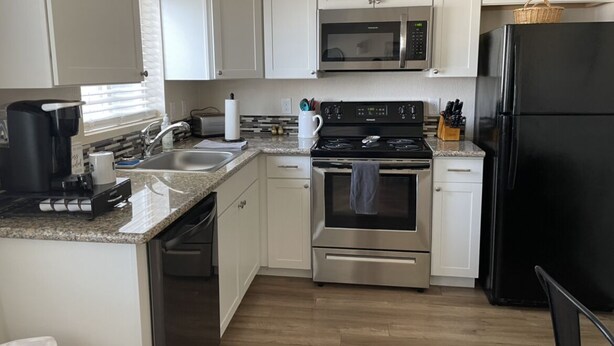 Una cocina compacta con gabinetes blancos, un microondas de acero inoxidable, un refrigerador negro y una estufa a gas.