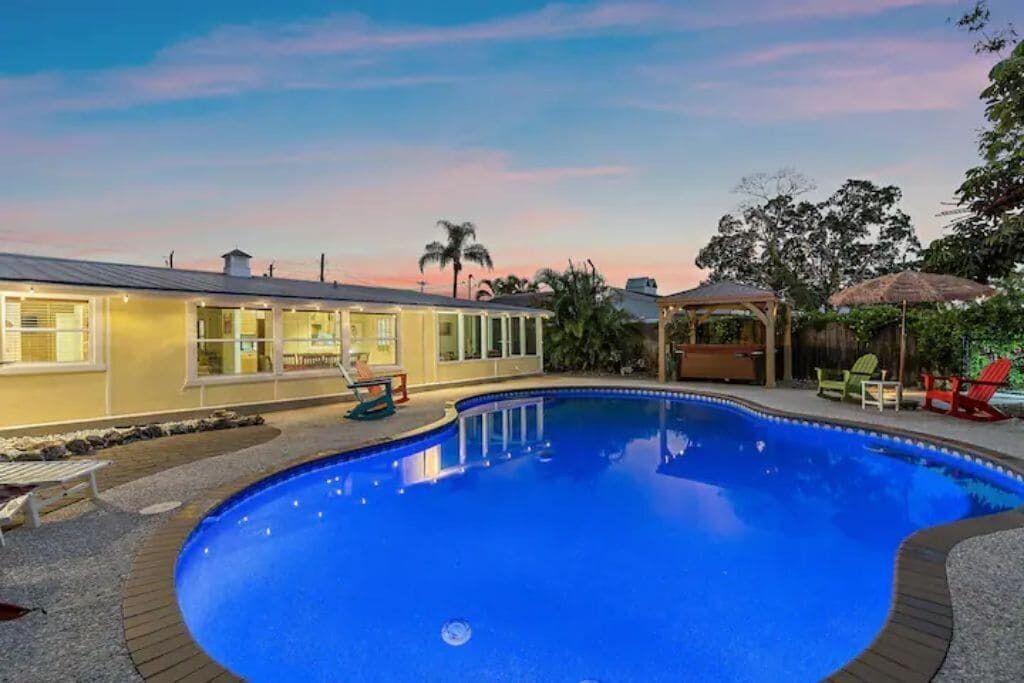 A swimming pool with a wooden deck, lounge chairs, and a covered seating area.