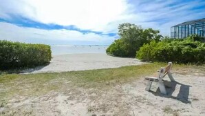 Una playa con un banco, un edificio de cristal y cielo despejado.