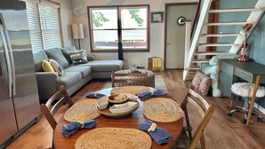 A modern living room with a wooden dining table, a sofa, and a staircase. - Island Sandbar retreat with sunset views, water toys and more! Boat-Only Access (Wolcott)