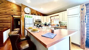 A kitchen with a wooden accent wall, a clock, a refrigerator, a sink, and bar stools. - Relax in Nature's Beauty: Private Log Cabin w/ two Spacious, Open Living Areas (Shipman)