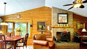 A cozy log cabin interior with a dining area, leather sofas, a fireplace, and a ceiling fan. - Relax in Nature's Beauty: Private Log Cabin w/ two Spacious, Open Living Areas (Shipman)