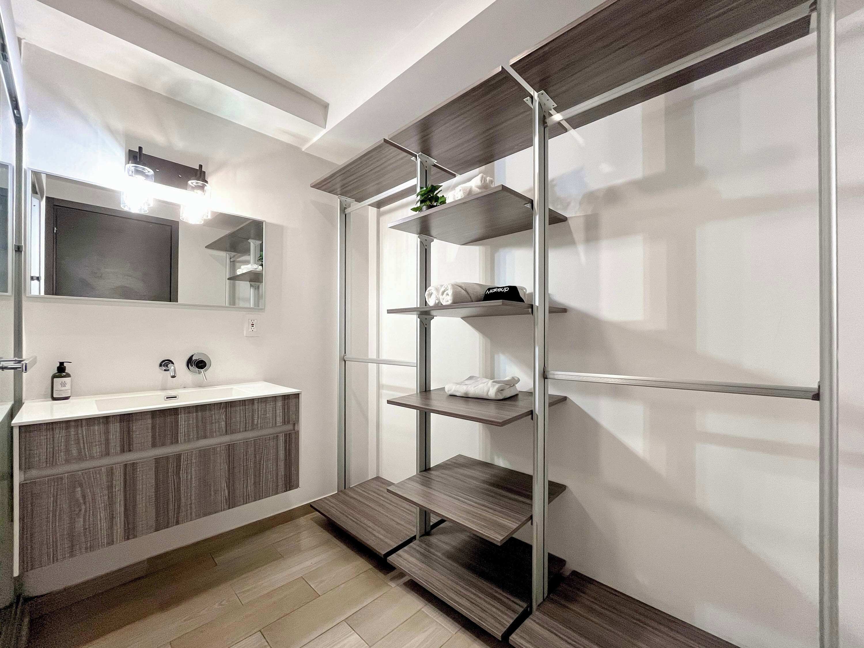 Een moderne badkamer met een houten wastafelmeubel, een spiegel en ingebouwde planken voor opbergruimte.