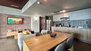 Una cocina moderna con una mesa de comedor de madera y sillas grises, un microondas integrado y una pared de ladrillo con una obra de arte colorida.
