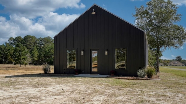 A modern, dark-colored barn-style building with a sloped roof, large windows, and a small porch area. - Brand New, Beautifully Appointed, Country Cottage! (Lindale)
