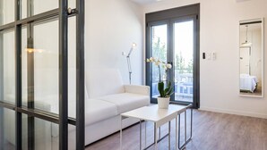A modern hotel room with a white sofa, a small table, a potted plant, and a large window offering a view of the outdoors. - Emily in Athens - Chic central flat w/green terrace b/n Syntagma & Monastiraki (Athina)