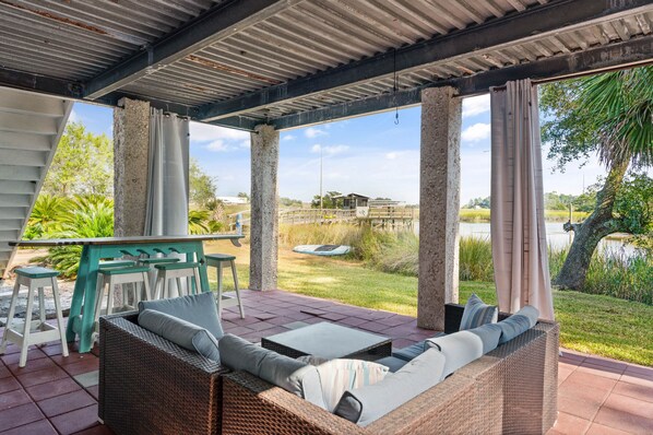 A covered outdoor seating area with wicker furniture and a view of a lake and greenery.