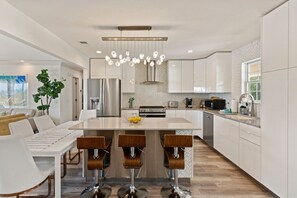 A modern kitchen with a central island, bar stools, stainless steel appliances, and a herringbone-patterned backsplash.