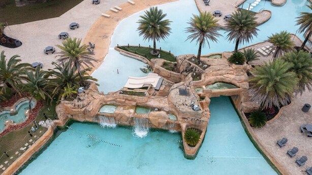 A pool area with palm trees, lounge chairs, and a waterfall feature. - Wharf 703|Waterfront View|2 bedroom|Pool|sleeps 8! (Orange Beach)