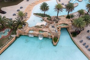 A pool area with palm trees, lounge chairs, and a waterfall feature. - Snowbird Rates|Wharf 703|Waterfront View|sleeps 8! (Orange Beach)