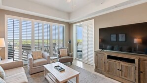 A spacious living room with a large TV, comfortable seating, and a balcony with sliding doors. - Wharf 703|Waterfront View|2 bedroom|Pool|sleeps 8! (Orange Beach)
