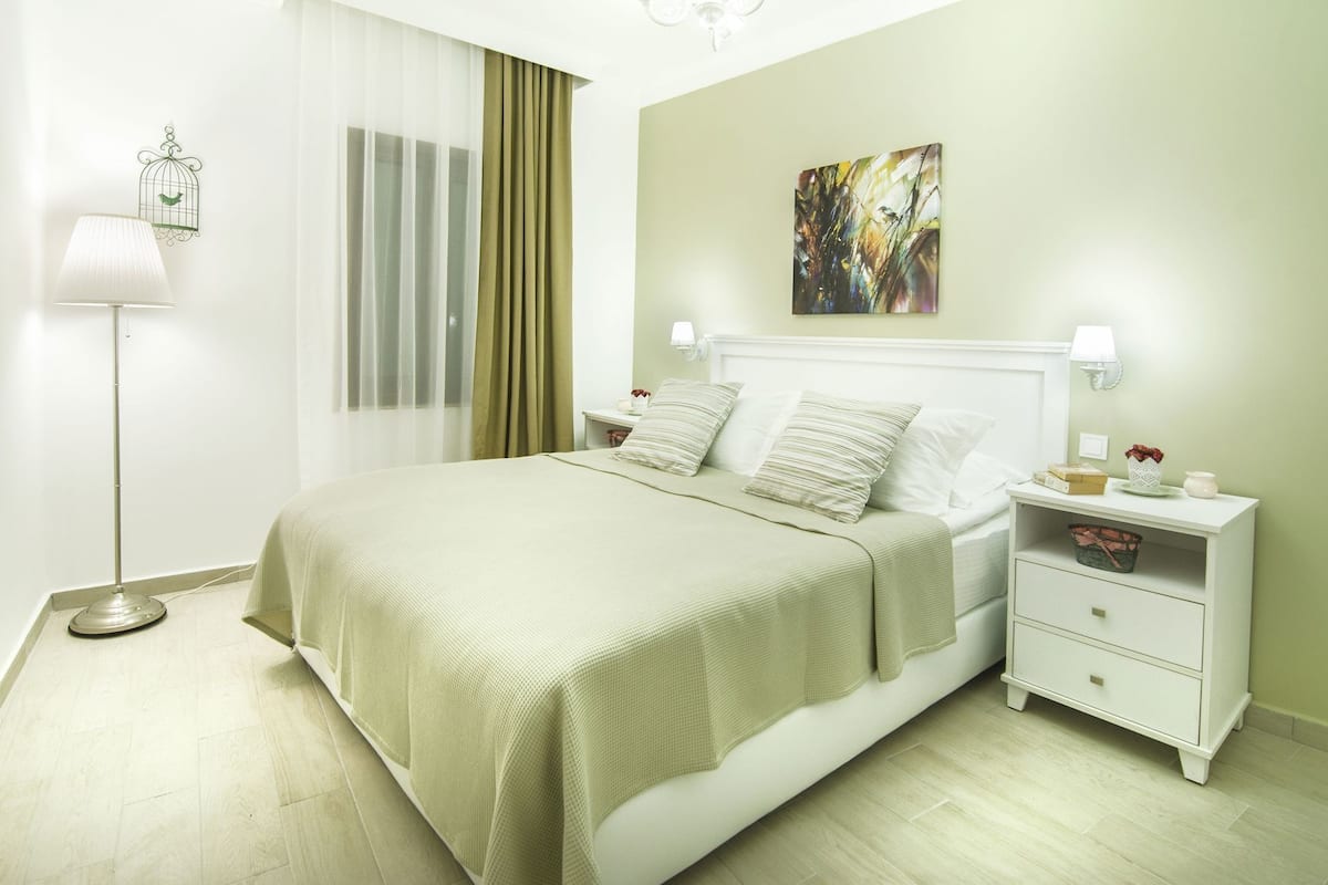 A neatly arranged bedroom with a bed, bedside tables, a lamp, and a wall art piece.