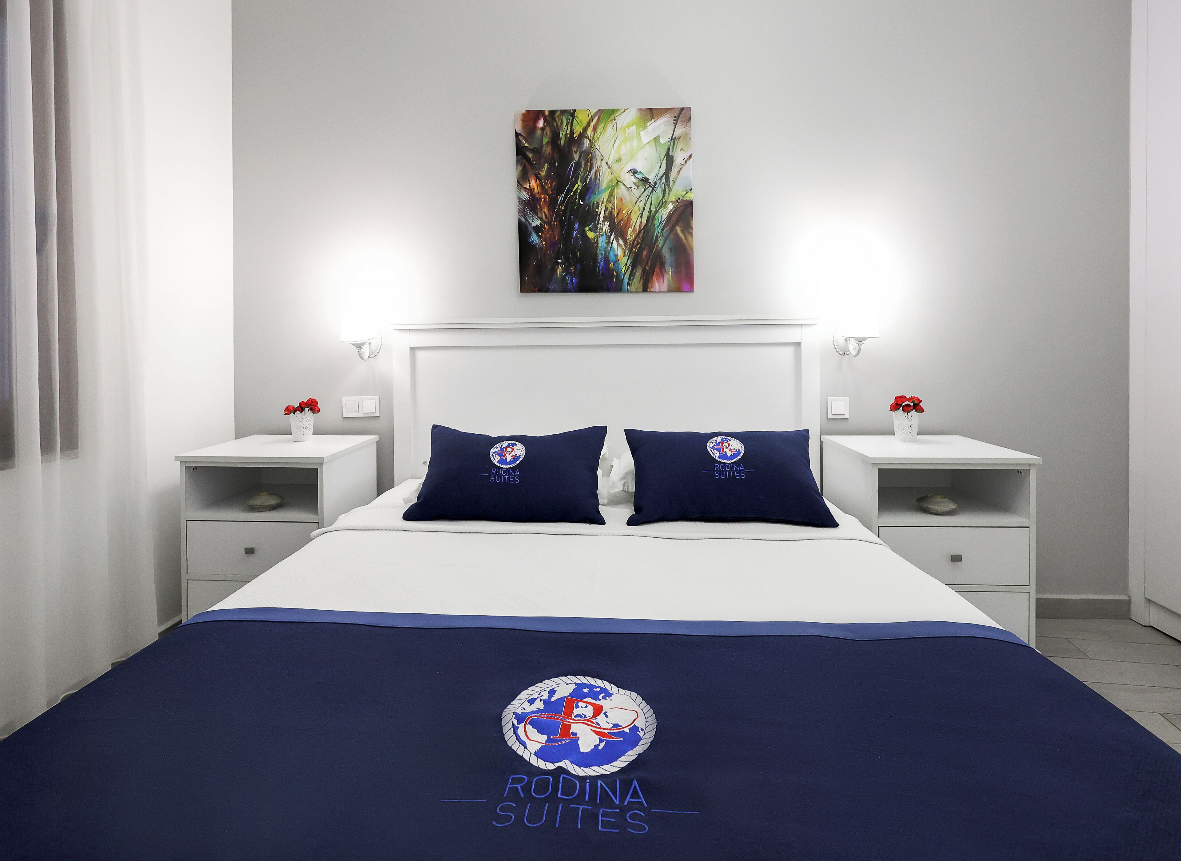 Une chambre d’hôtel avec un lit, deux tables de chevet, un tableau et un logo sur la couvre-lit.