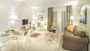 A modern living room with a sofa, a dining table set for two, a coffee table, and a TV. - Rodina Suites (Kusadasi)