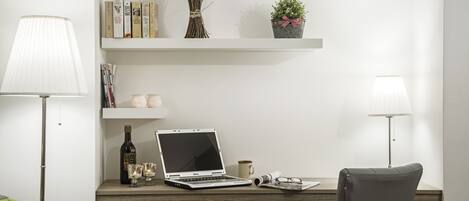A minimalist office setup with a laptop, desk, chair, lamps, and decorative items.