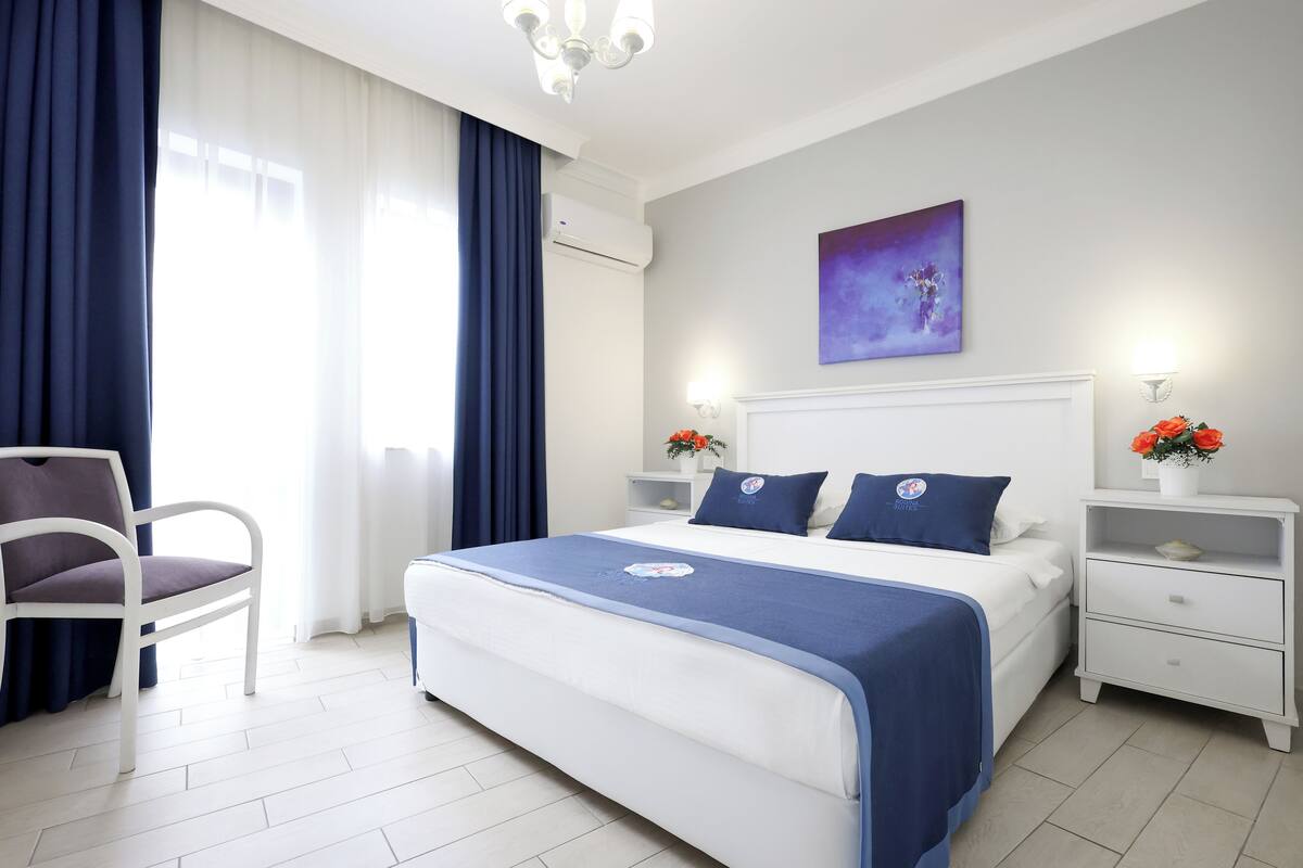 A modern bedroom with a large bed, a chair, a nightstand with a lamp, and a wall-mounted painting.