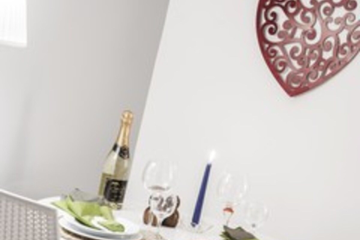 A dining table set with plates, glasses, a bottle of champagne, and a candle.