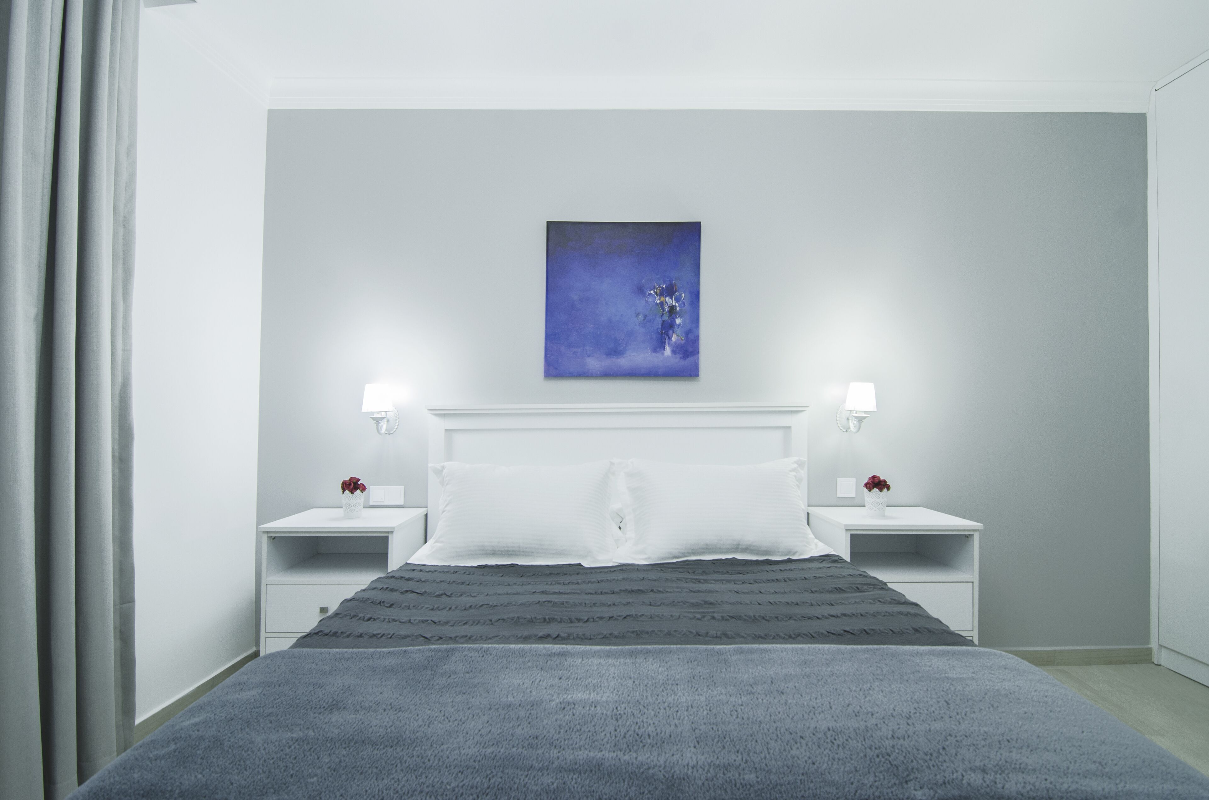 A modern hotel room with a large bed, two bedside tables, a nightstand, and a single wall-mounted painting.